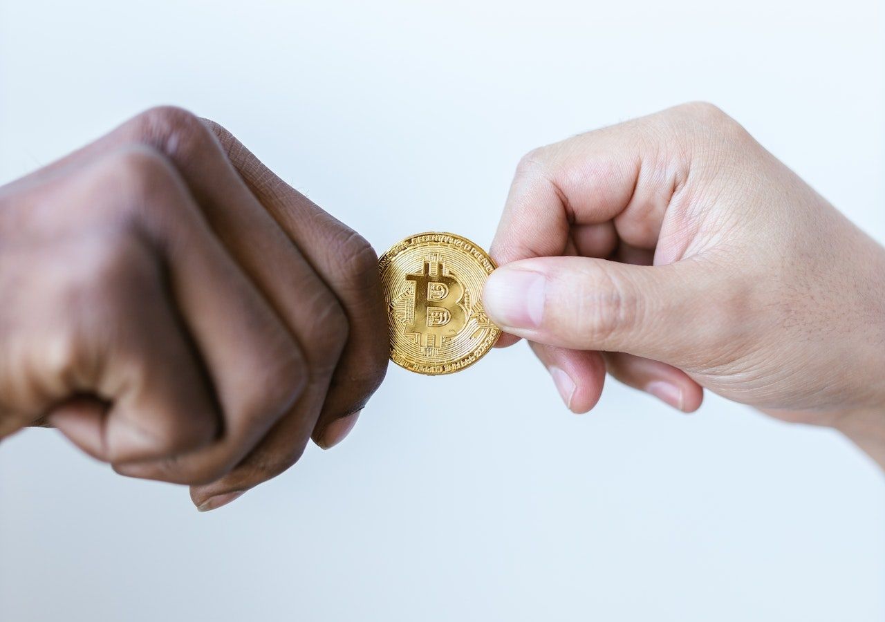 Two hands (black and white) exchanging a Bitcoin