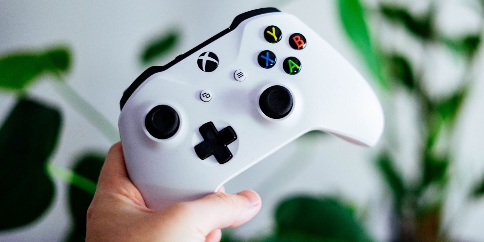 A photograph of a man holding up a white Xbox One Controller 