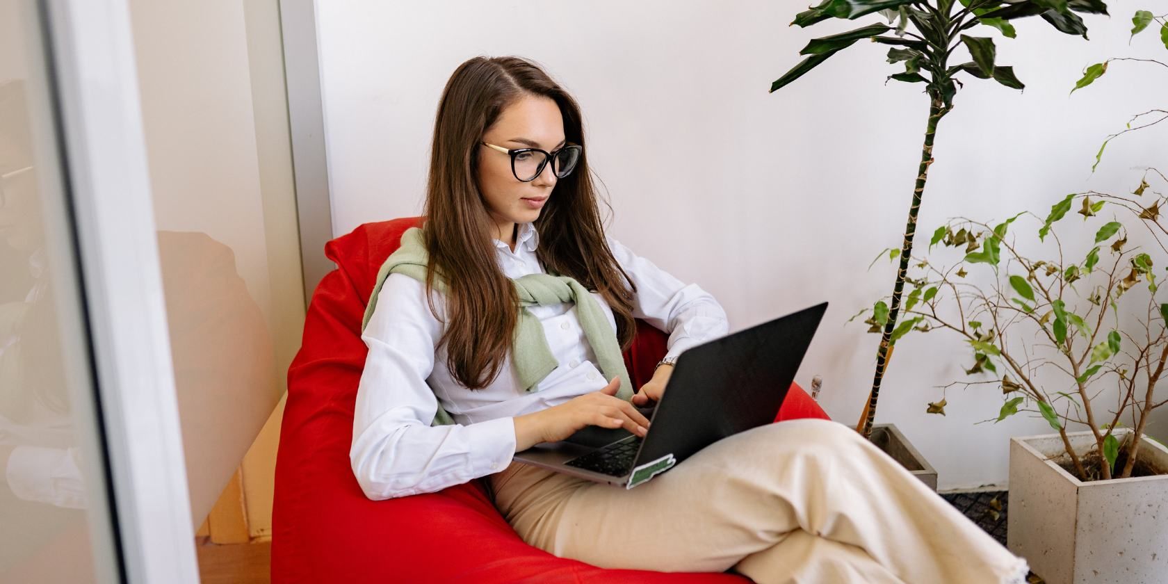 Femme aux cheveux noirs avec des lunettes tapant sur un ordinateur portable et assis sur un sac de haricots rouges