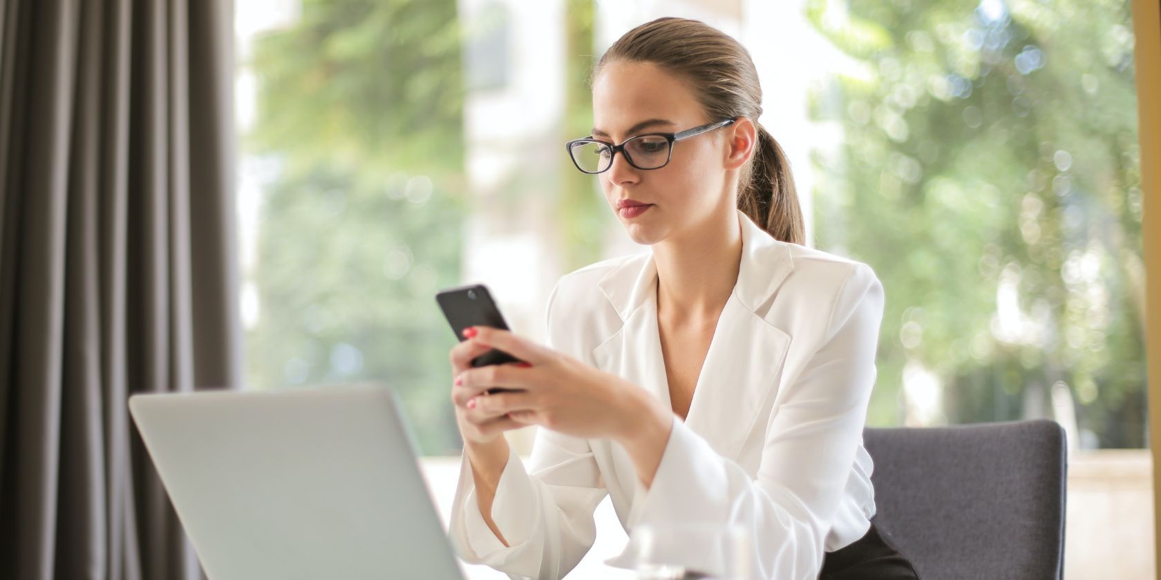 Serious looking woman in white blouse using a smartphone in the workplace