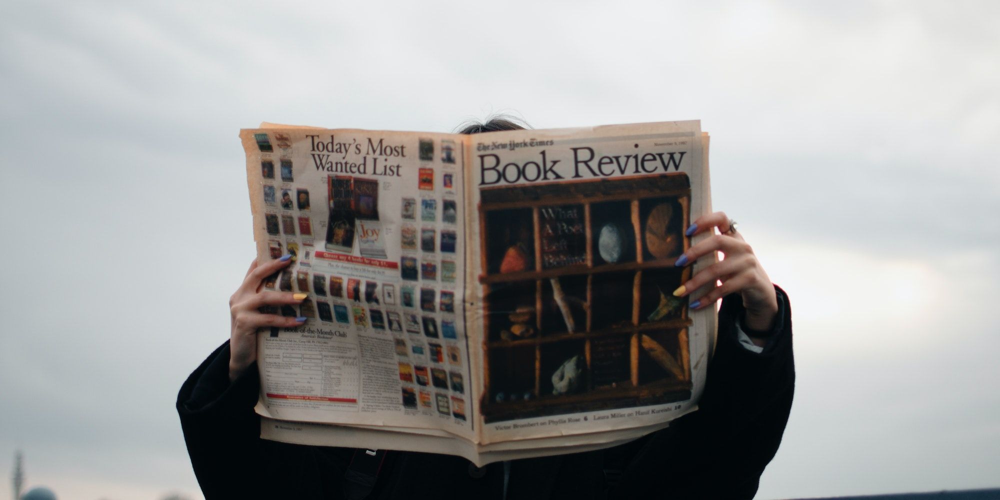 Person holding a newspaper cover with book reviews