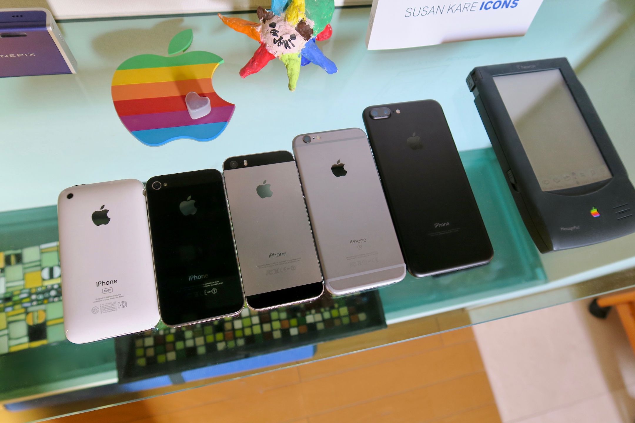 Several iPhones facedown beside an Apple Newton on a glass shelf