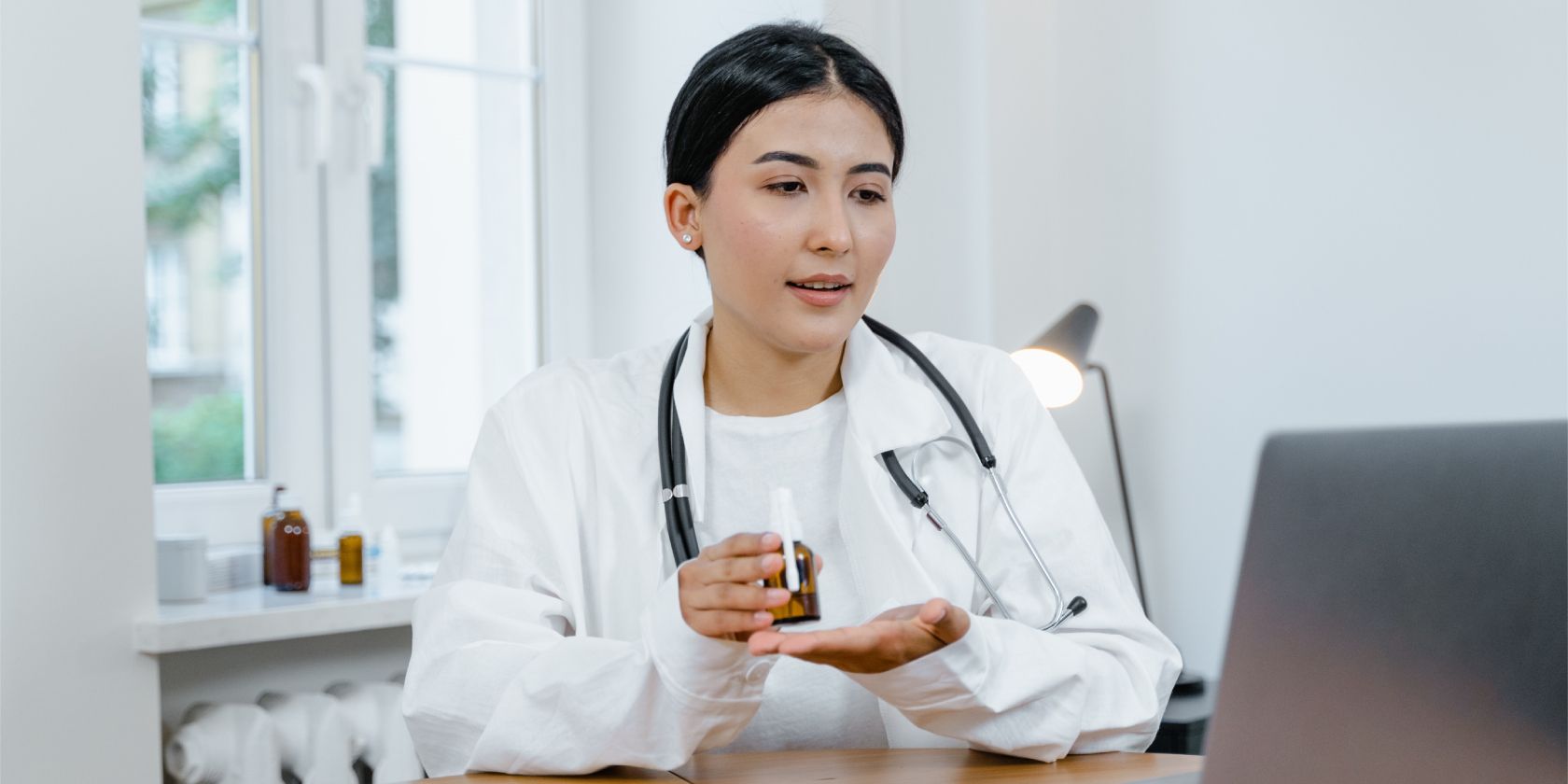 Woman doctor holding a medicine bottle in front of computer
