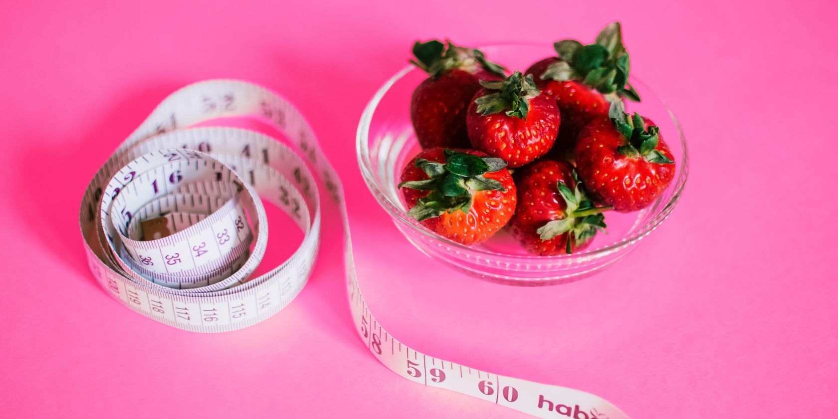 Waist measuring tape and bowl of strawberries on pink background