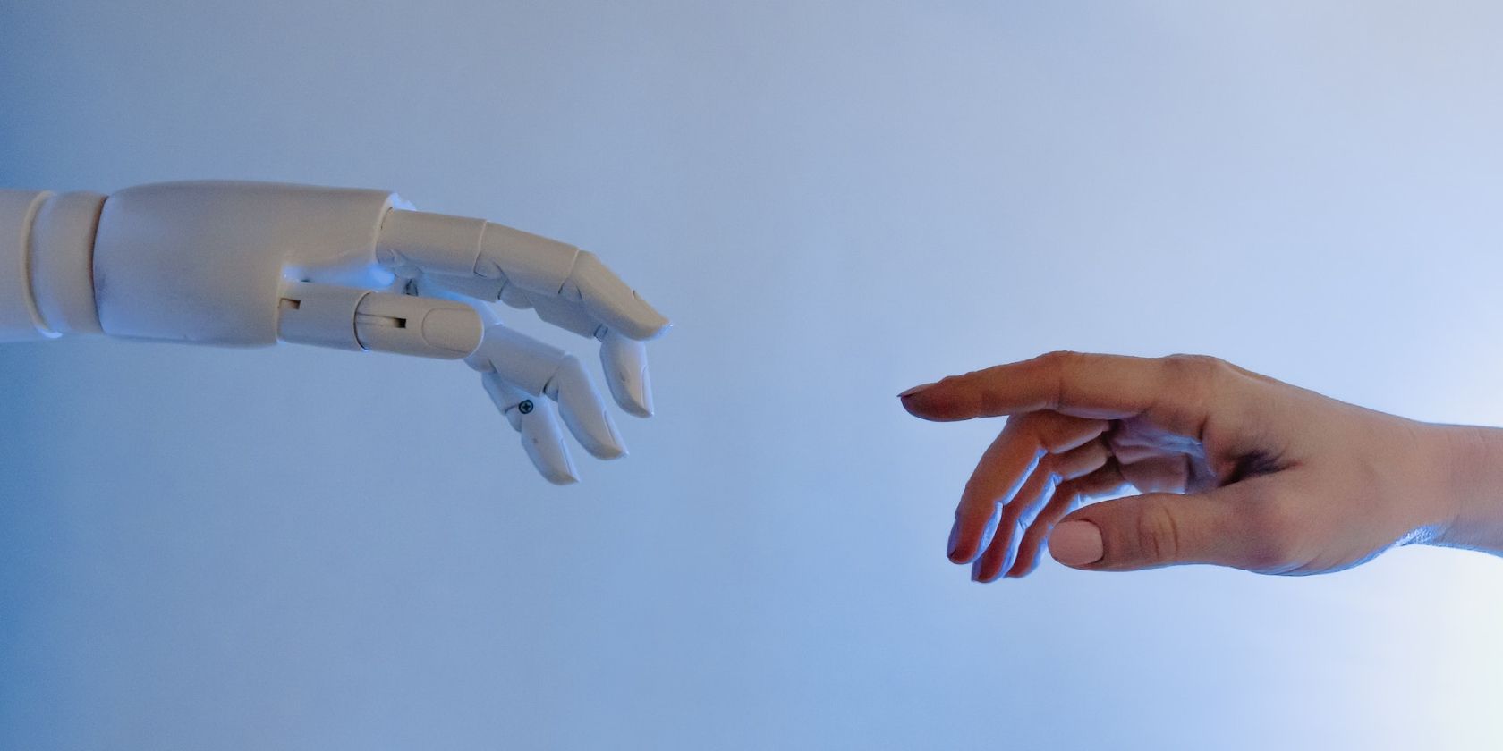 White robotic arm reaching out to human hand in front of a blue surface