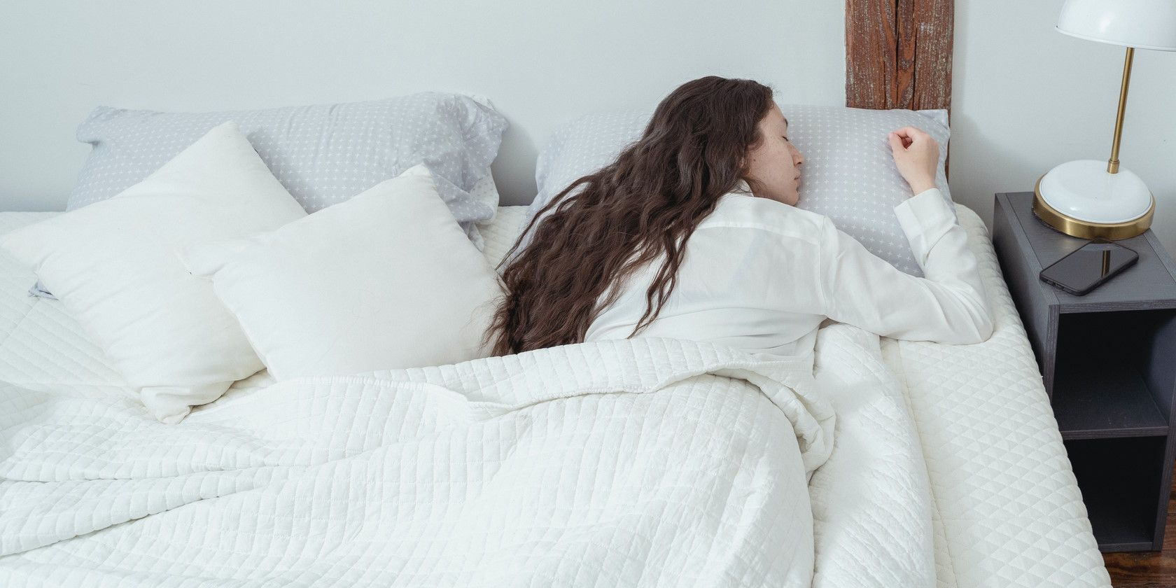 woman lying in bed and sleeping on stomach covered by white blanket