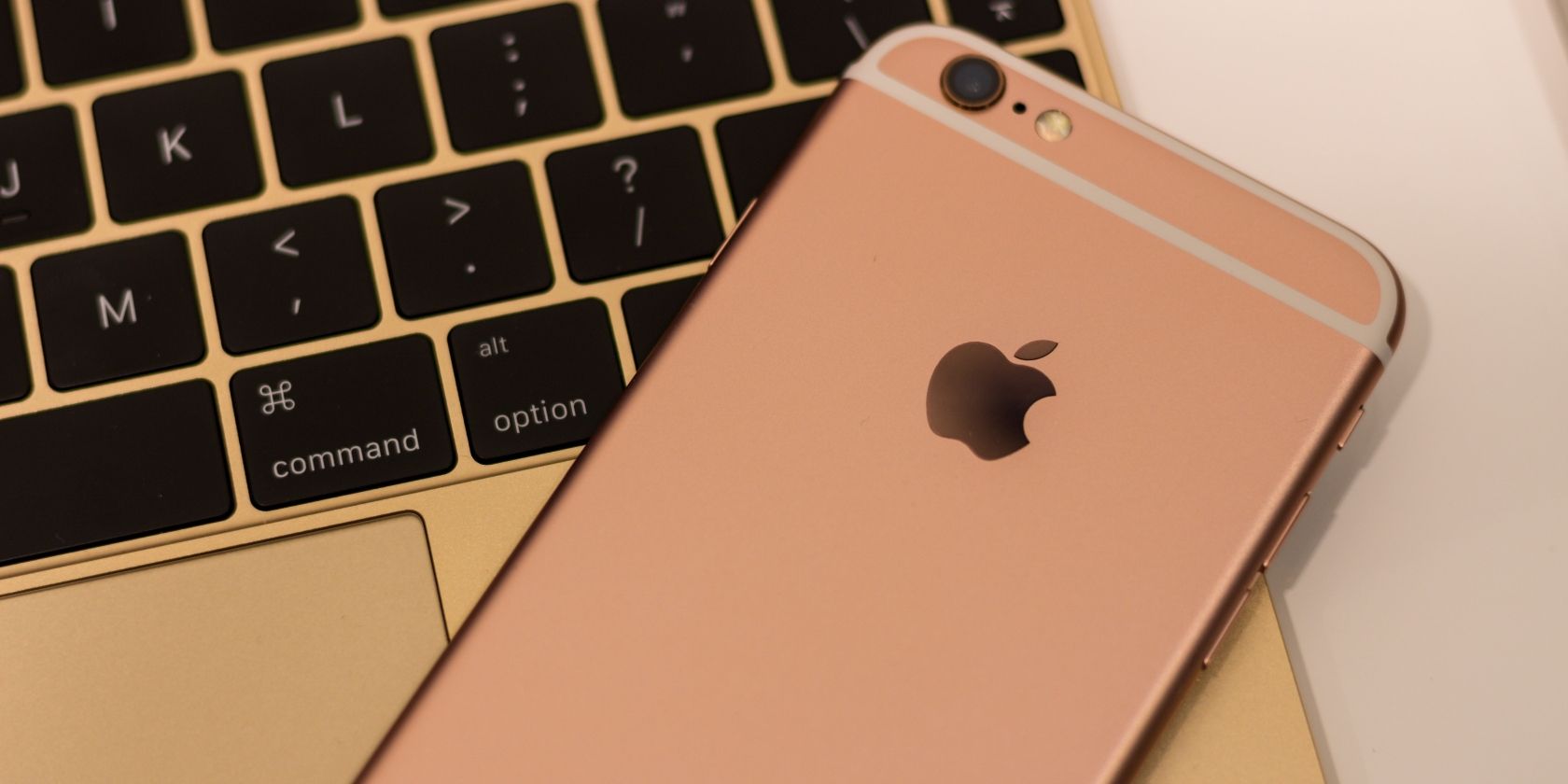 A gold iPhone on top of a gold MacBook