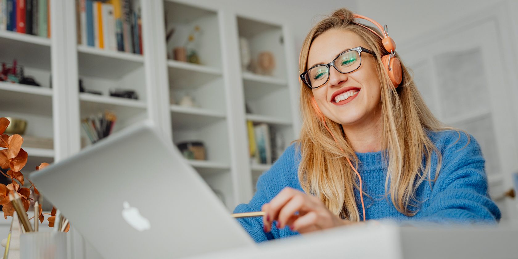 A happy woman listening to headphones while using a laptop