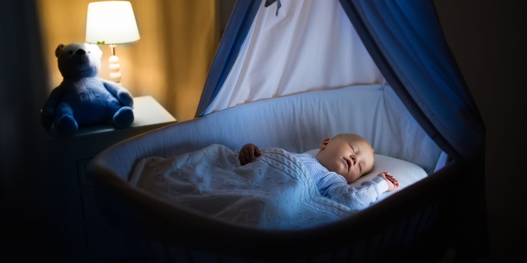 baby sleeping in blue bassinet with canopy at night