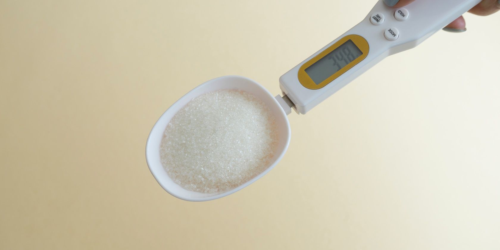 Person using a handheld spoon scale to measure sugar