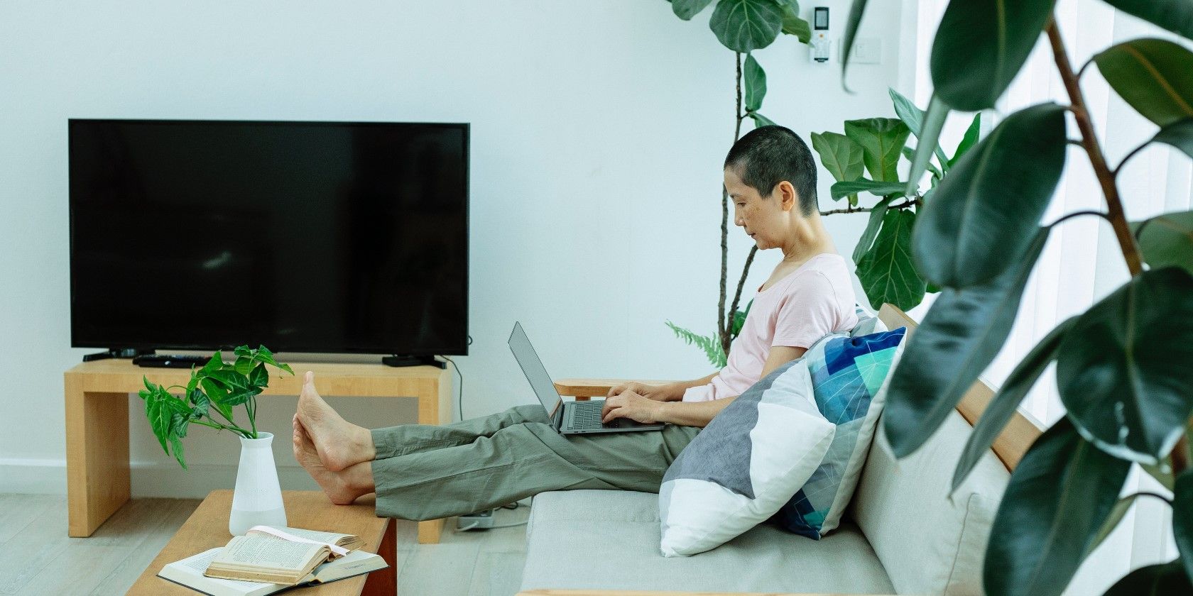 A woman with a laptop reclining on a couch near a TV 