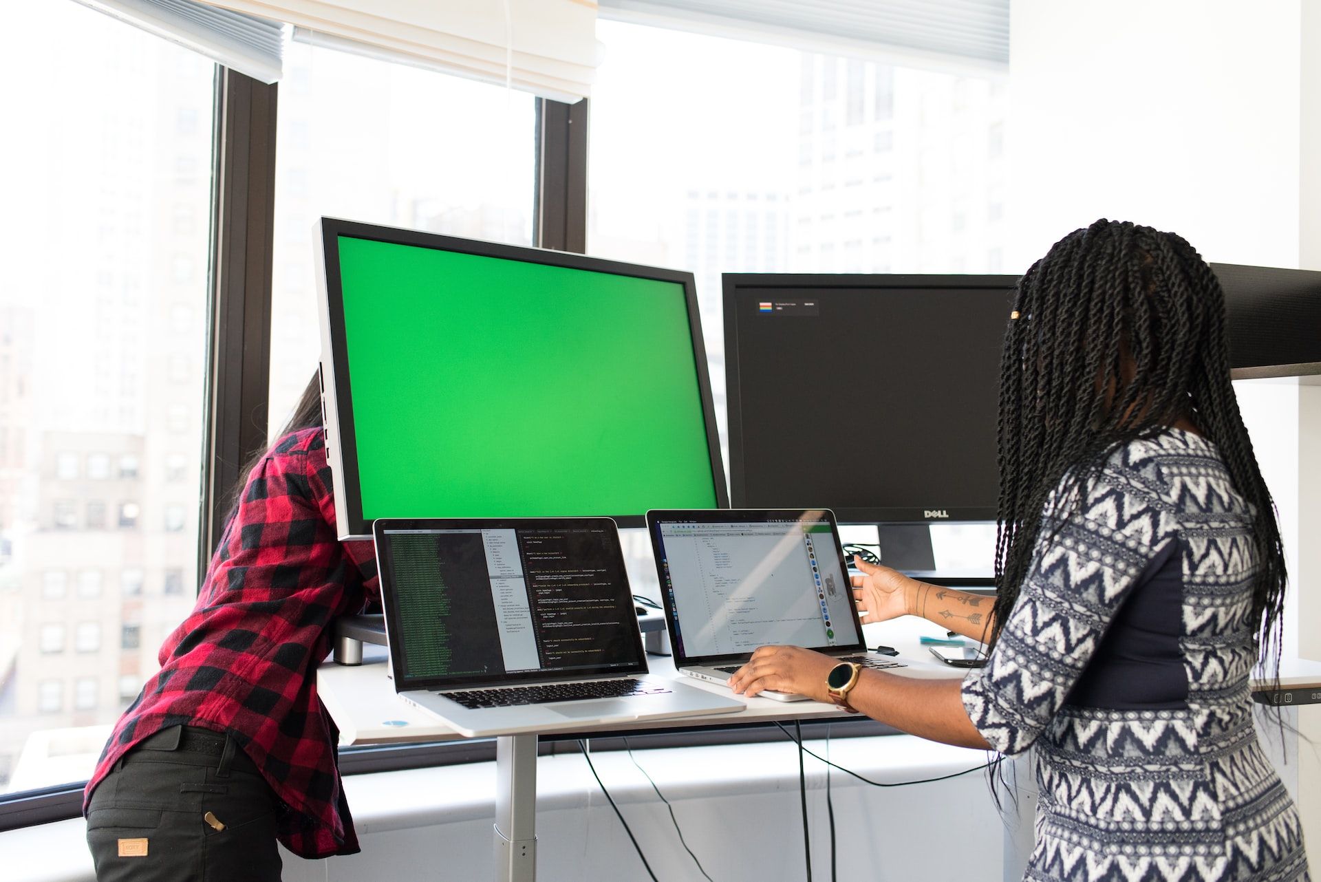 Pessoa olhando para um laptop e uma tela verde em um segundo monitor