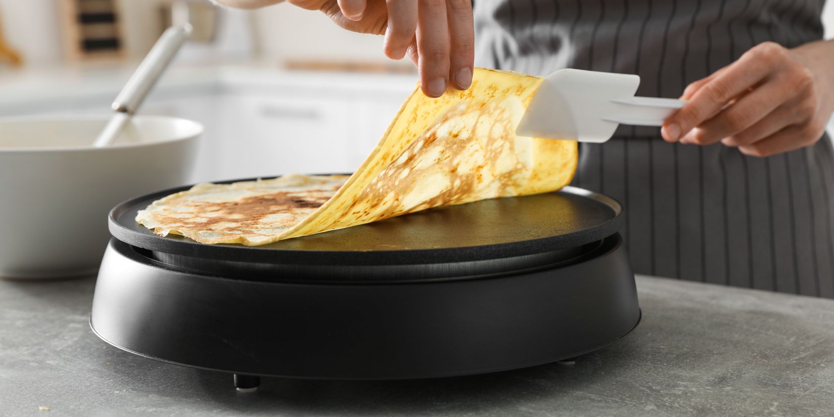 Person cooking crepe on electric pancake maker