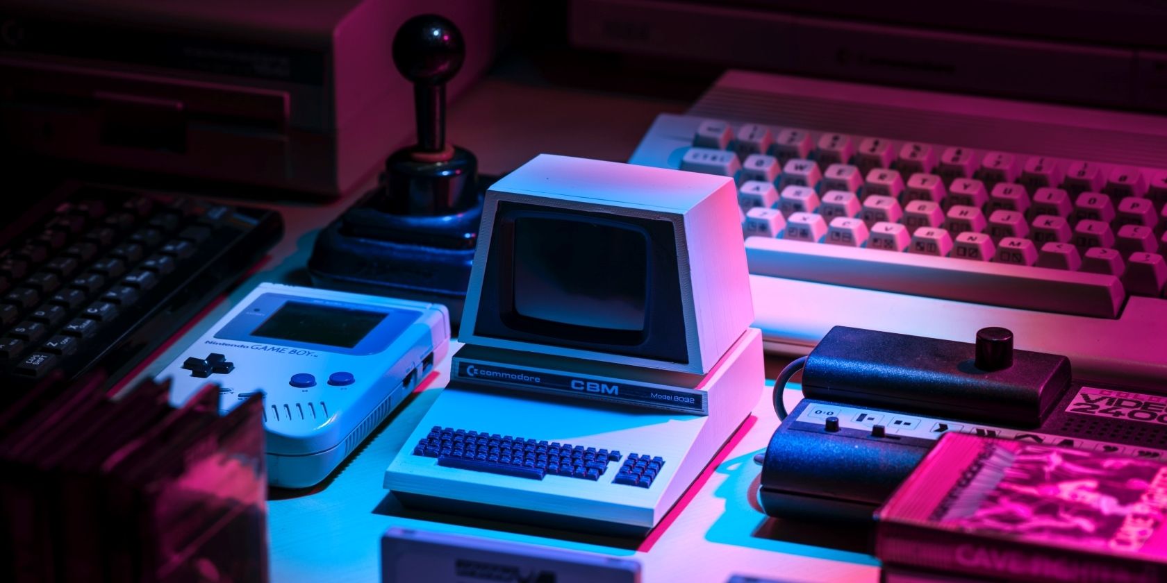 A photograph of a collection of retro gaming consoles and games held under a bright pink and blue light