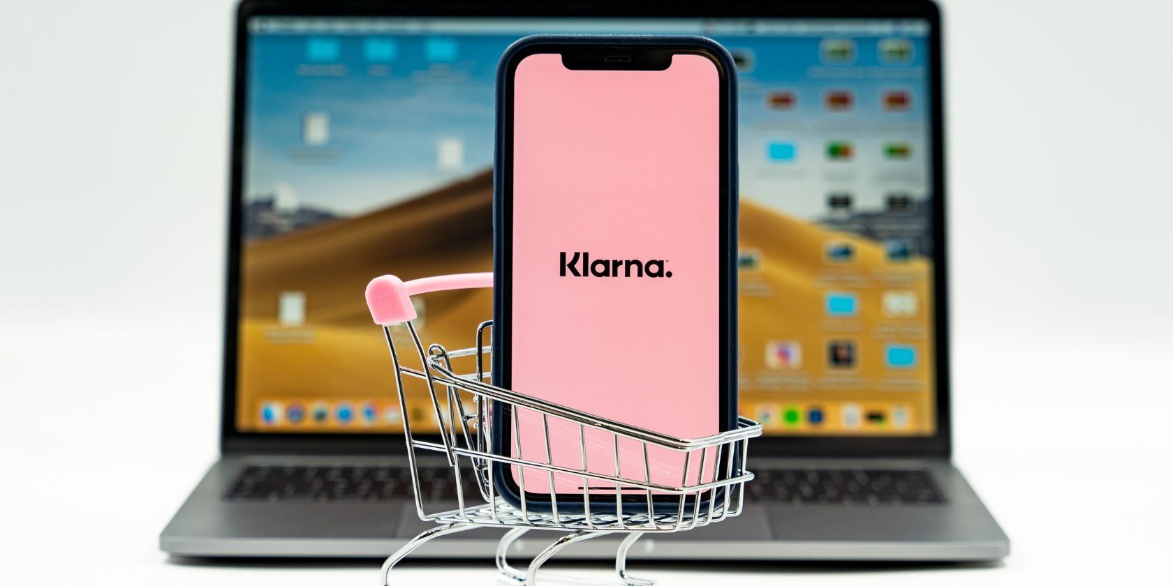 klarna app on smartphone in miniature trolley in front of macbook