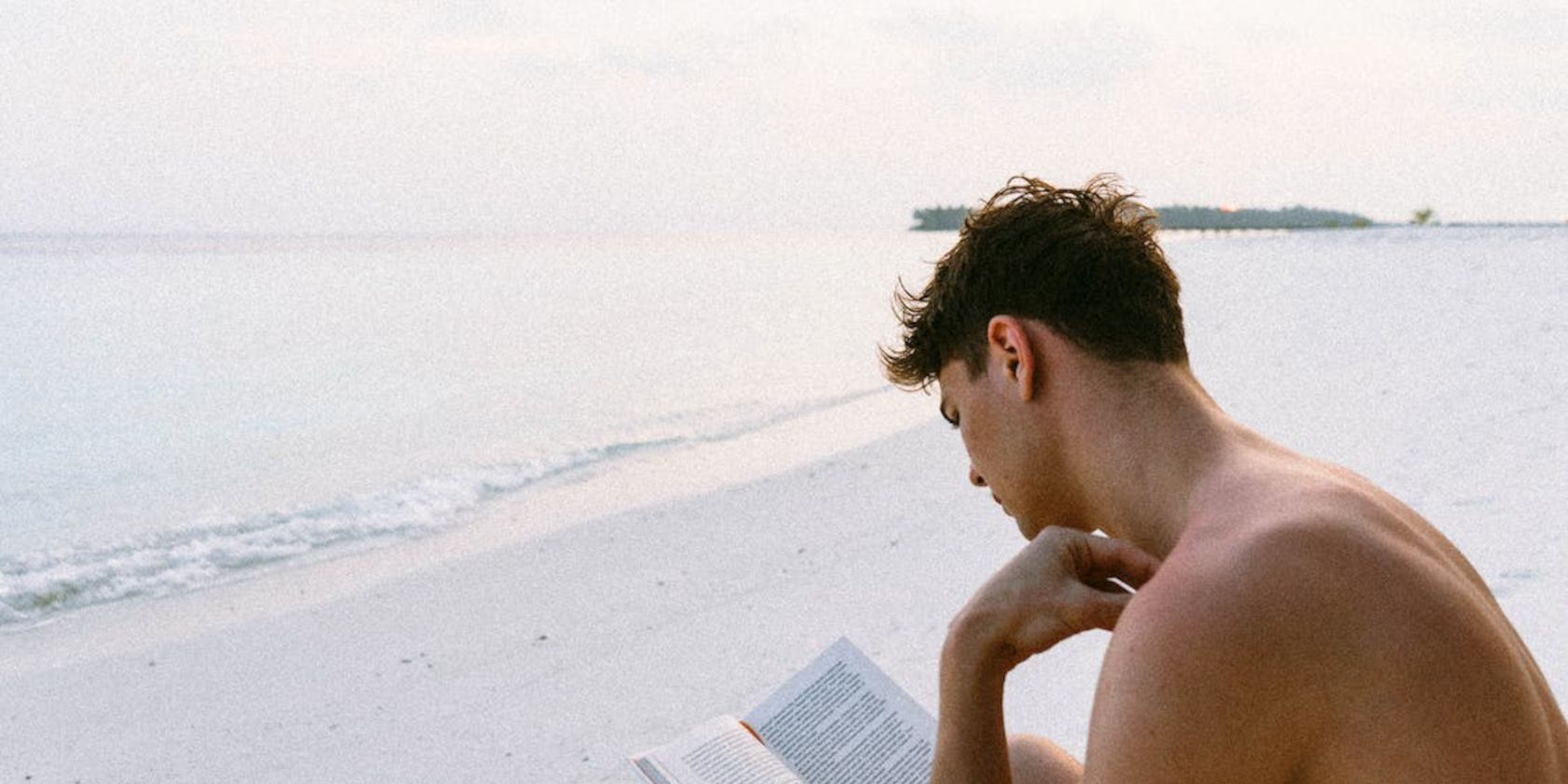 man on a beach reading a book