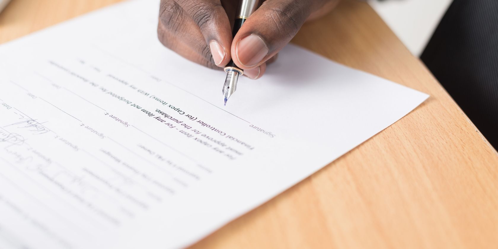 A man's hand holding a pen signing a document.