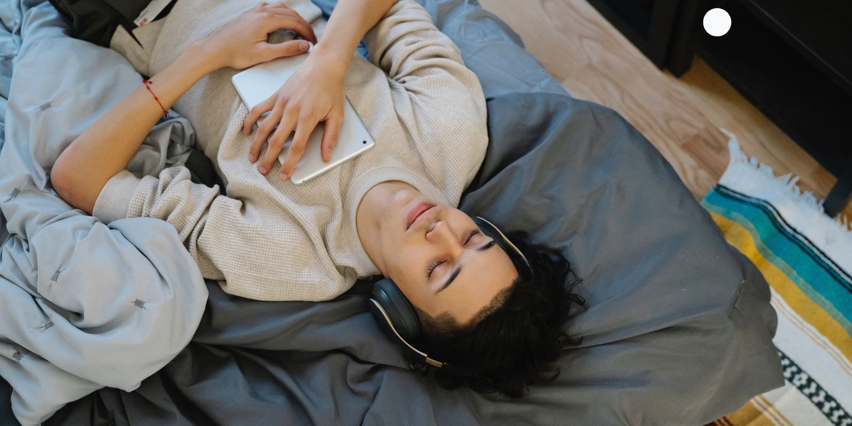 Man sleeping in bed while wearing headphones and holding a tablet to his chest 