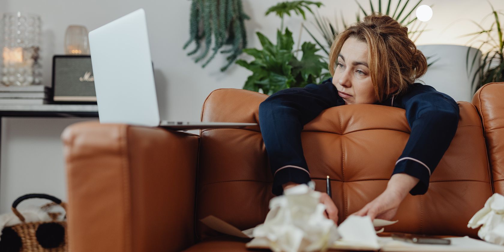 Stressed woman in pajamas lying on a couch and looking at her laptop   