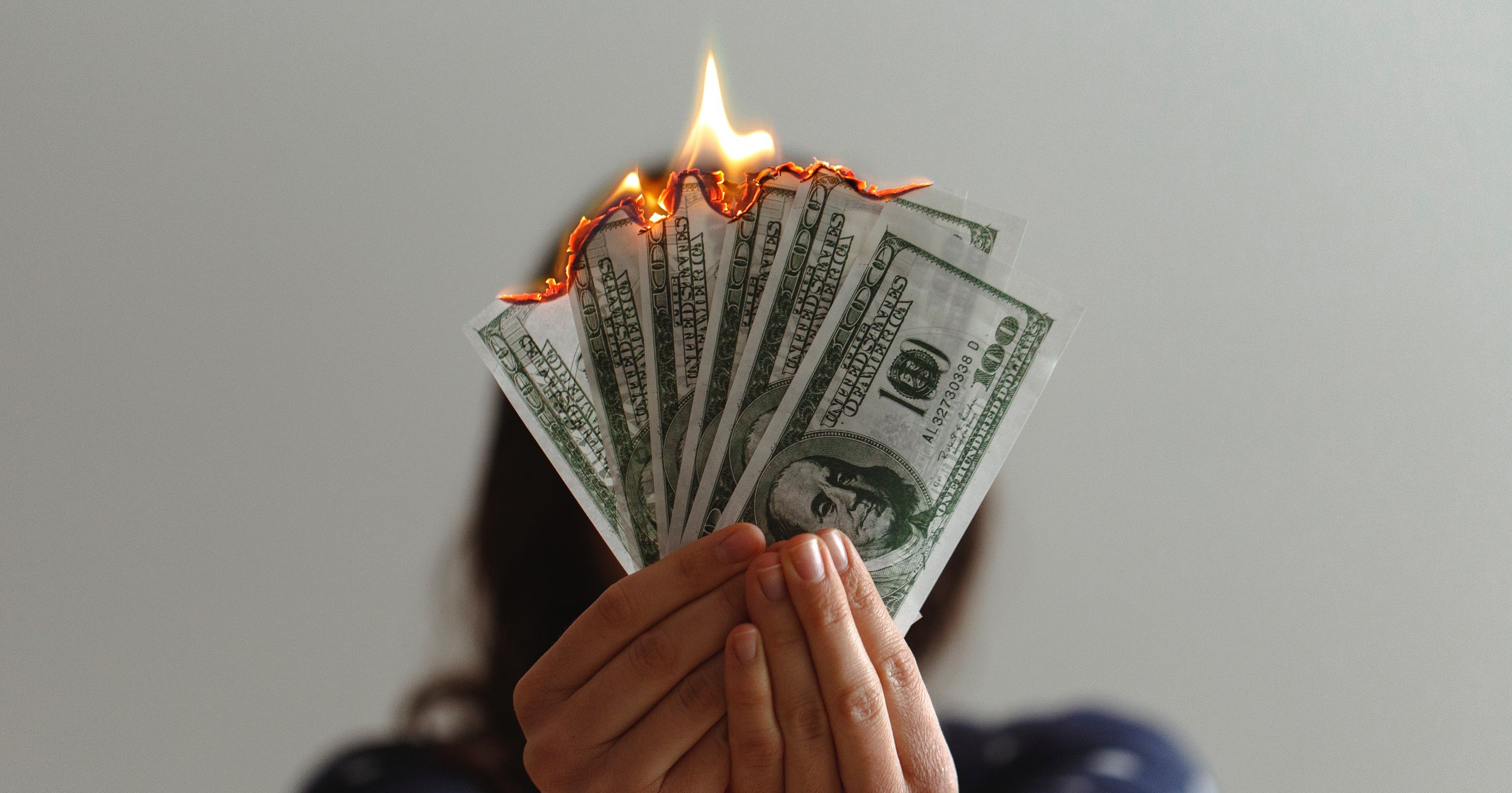 person holding hundred dollar bills on fire