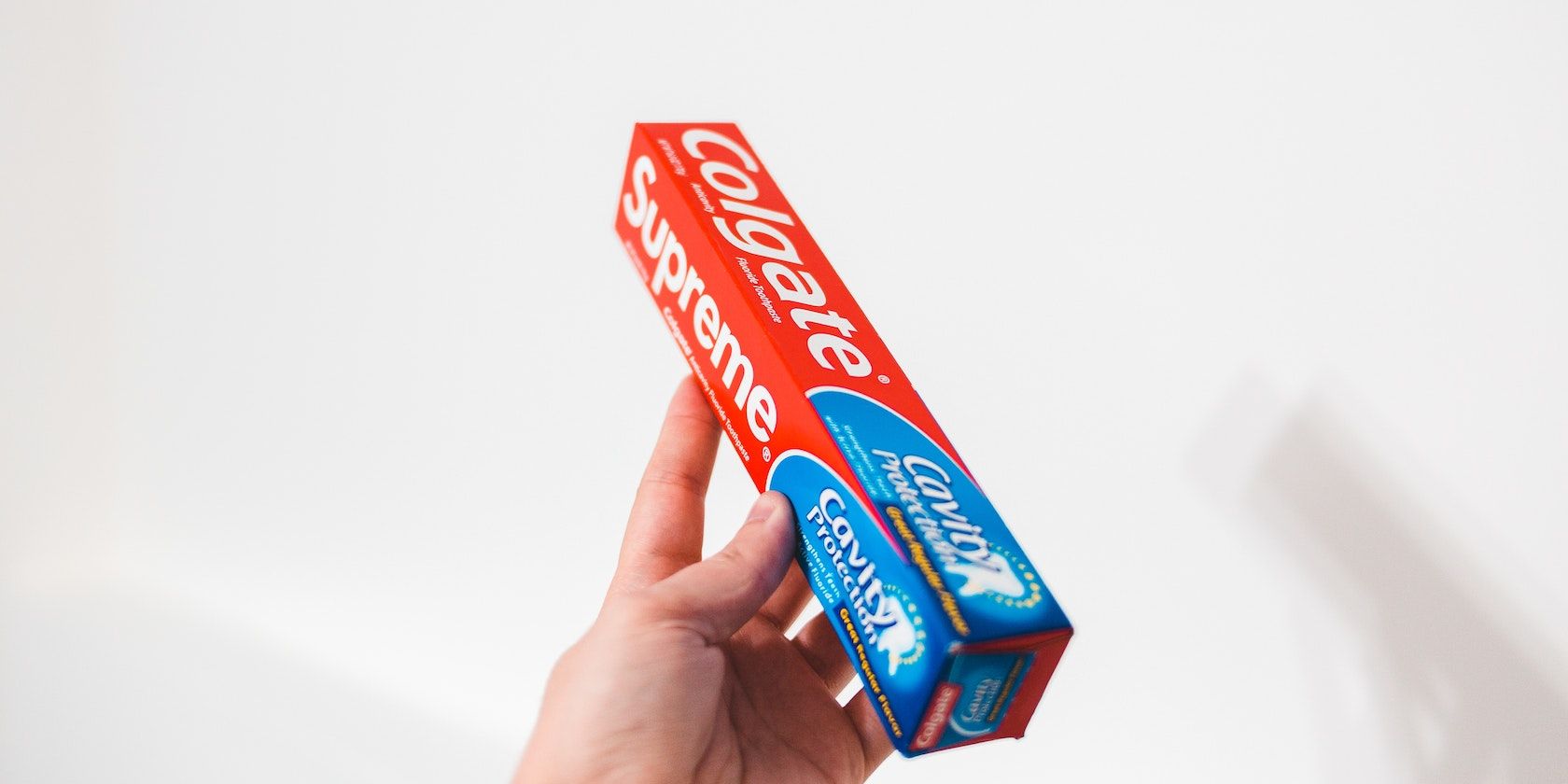 A hand holding a Colgate toothpaste box