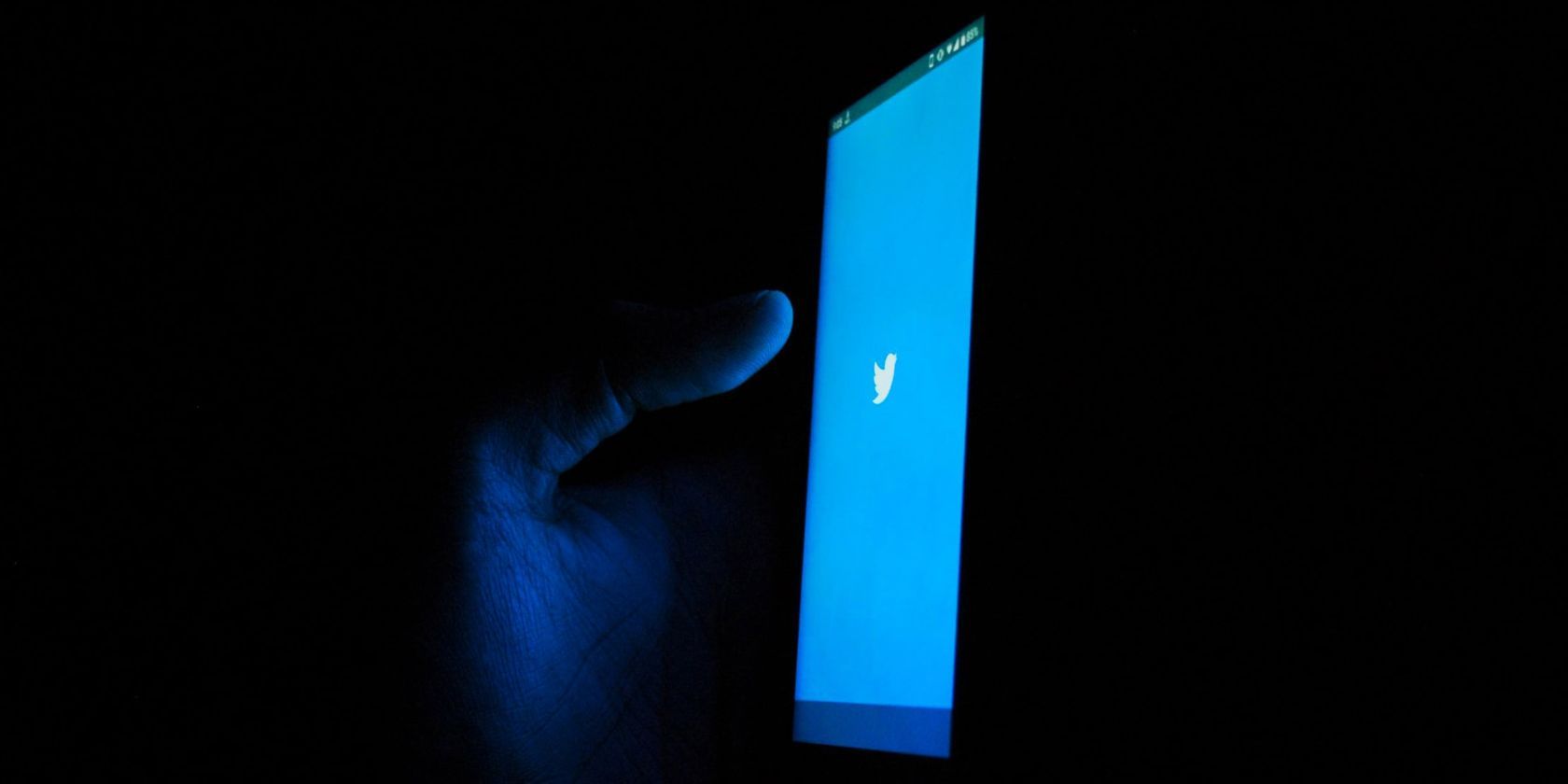 person in dark room using twitter app on smartphone