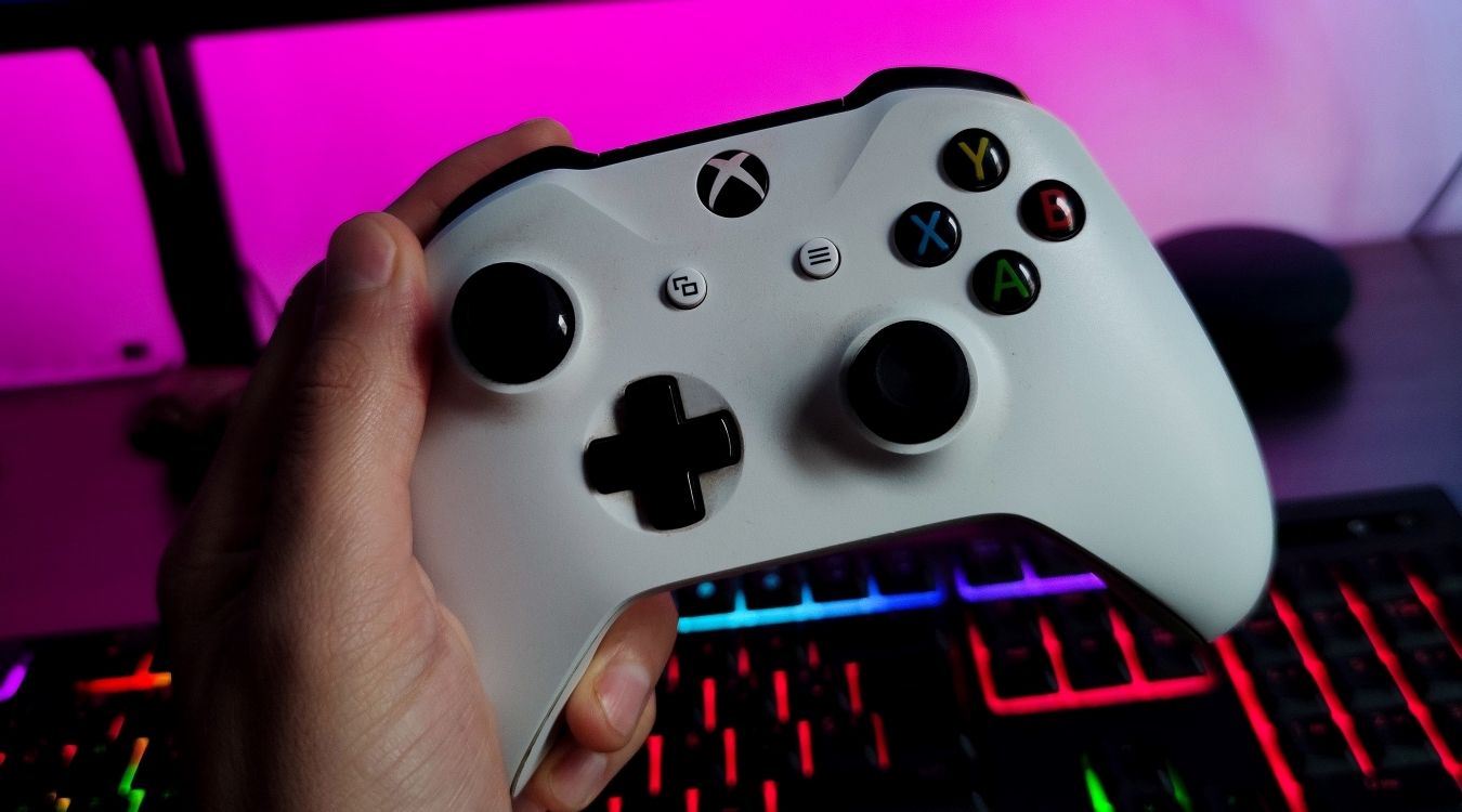 A photograph of a white Xbox One controller being held in front of a monitor 