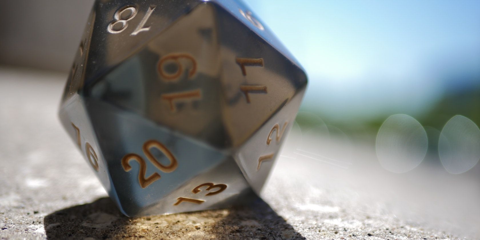 Translucent d20 die on a grainy surface