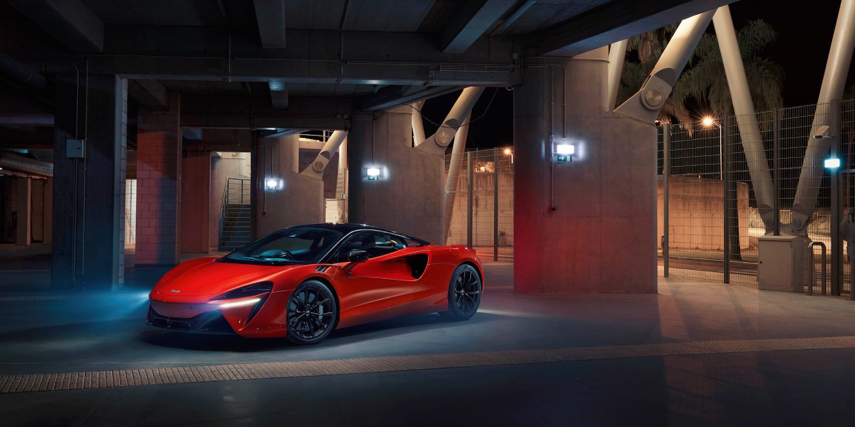 An orange 2023 McLaren Artura PHEV parked near a low-lit building