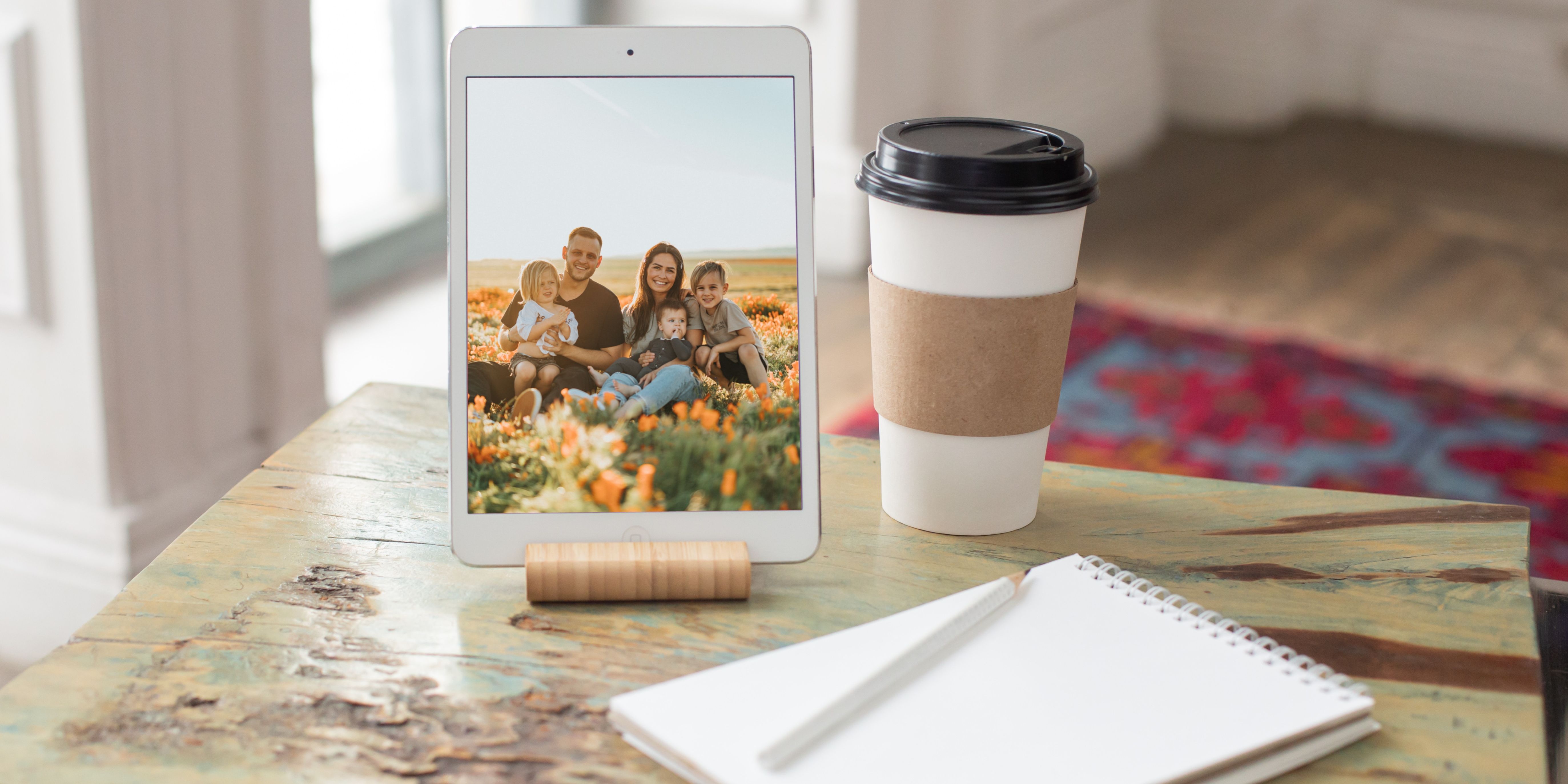iPad mini on a wooden table next to a cup of coffee and a notepad, displaying a family photo