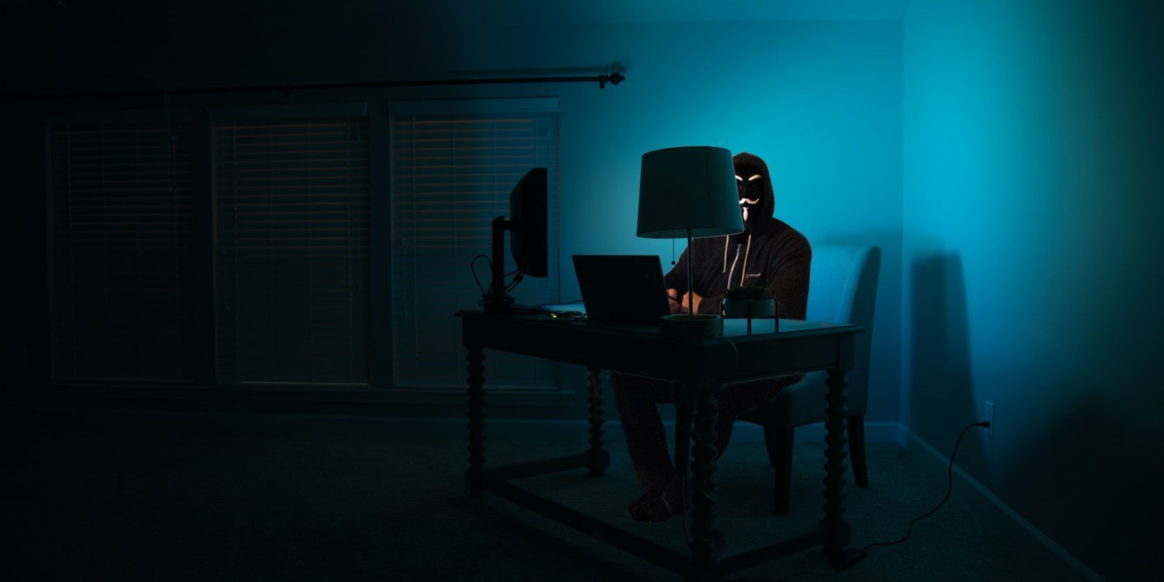 masked person sitting in dark room on computer