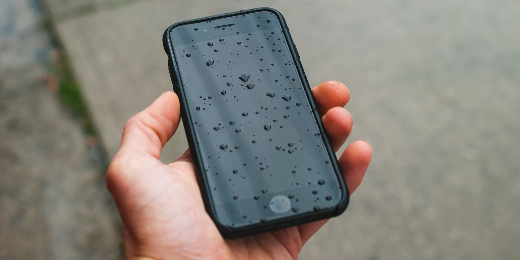 A hand holding a phone with droplets of water on the screen