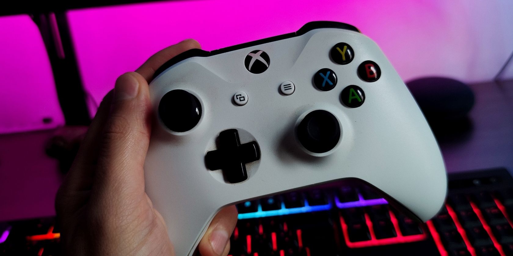 A photograph of someone holding a white Xbox Wireless Controller in front of a lit keyboard and monitor 