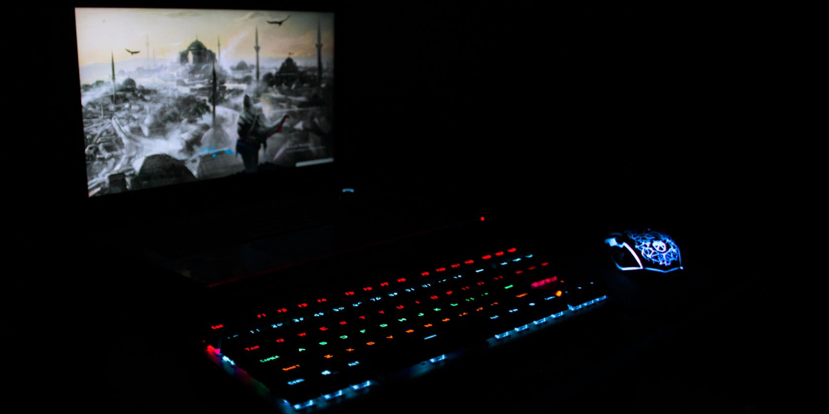 FPS game on screen in a dark room with a glowing pair of a keyboard and a mouse