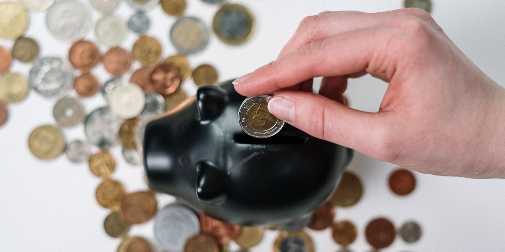 A person inserting a coin in a black piggy bank. 