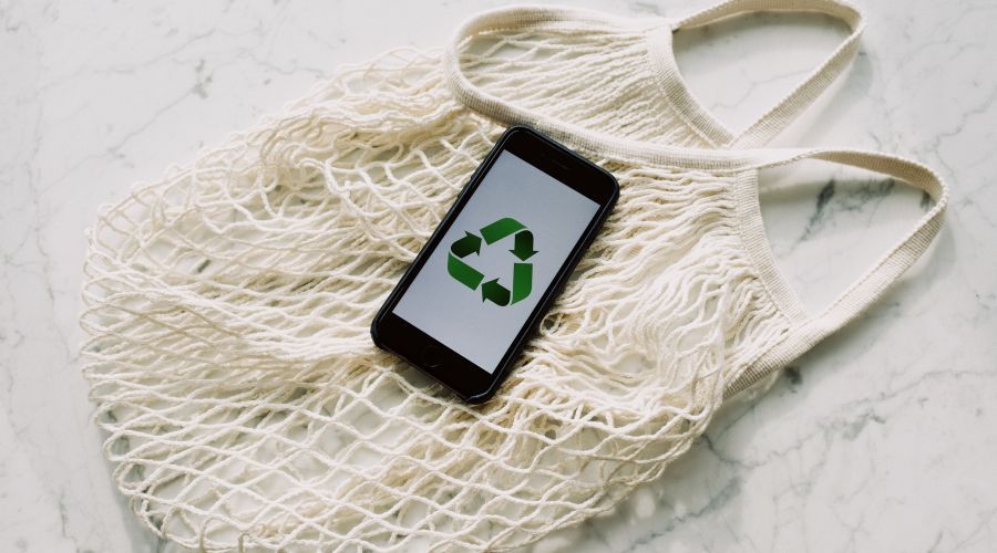 iPhone dengan simbol daur ulang hijau di tas jinjing