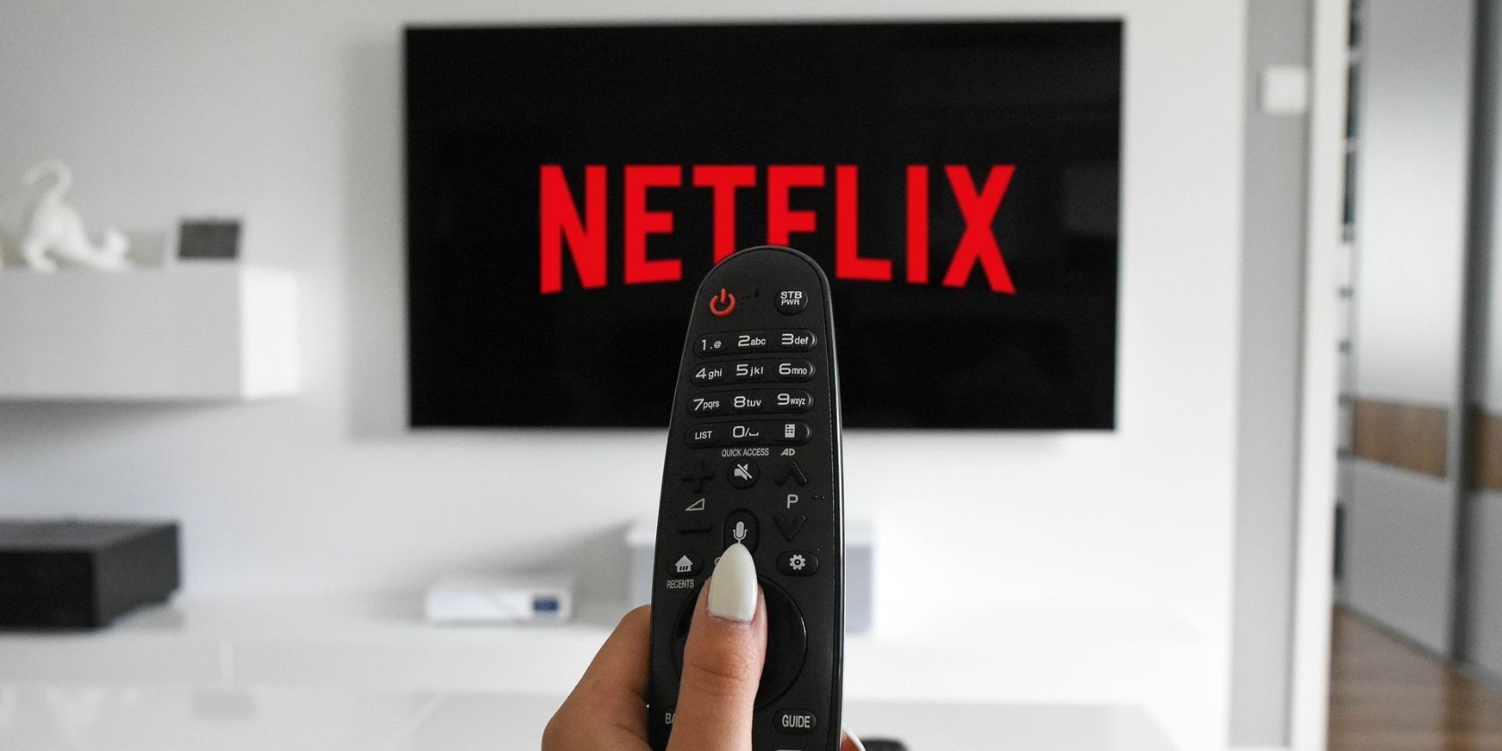 Một người phụ nữ đang cầm điều khiển TV trước TV đang tải Netflix