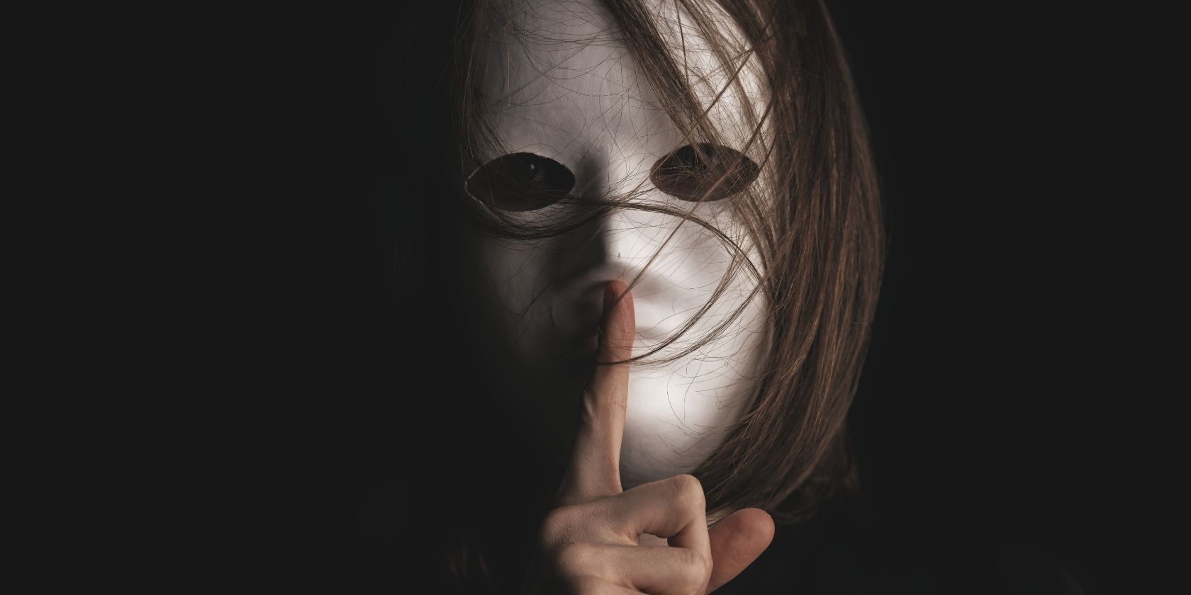 A person wearing a white mask with their finger on the lips of the mask