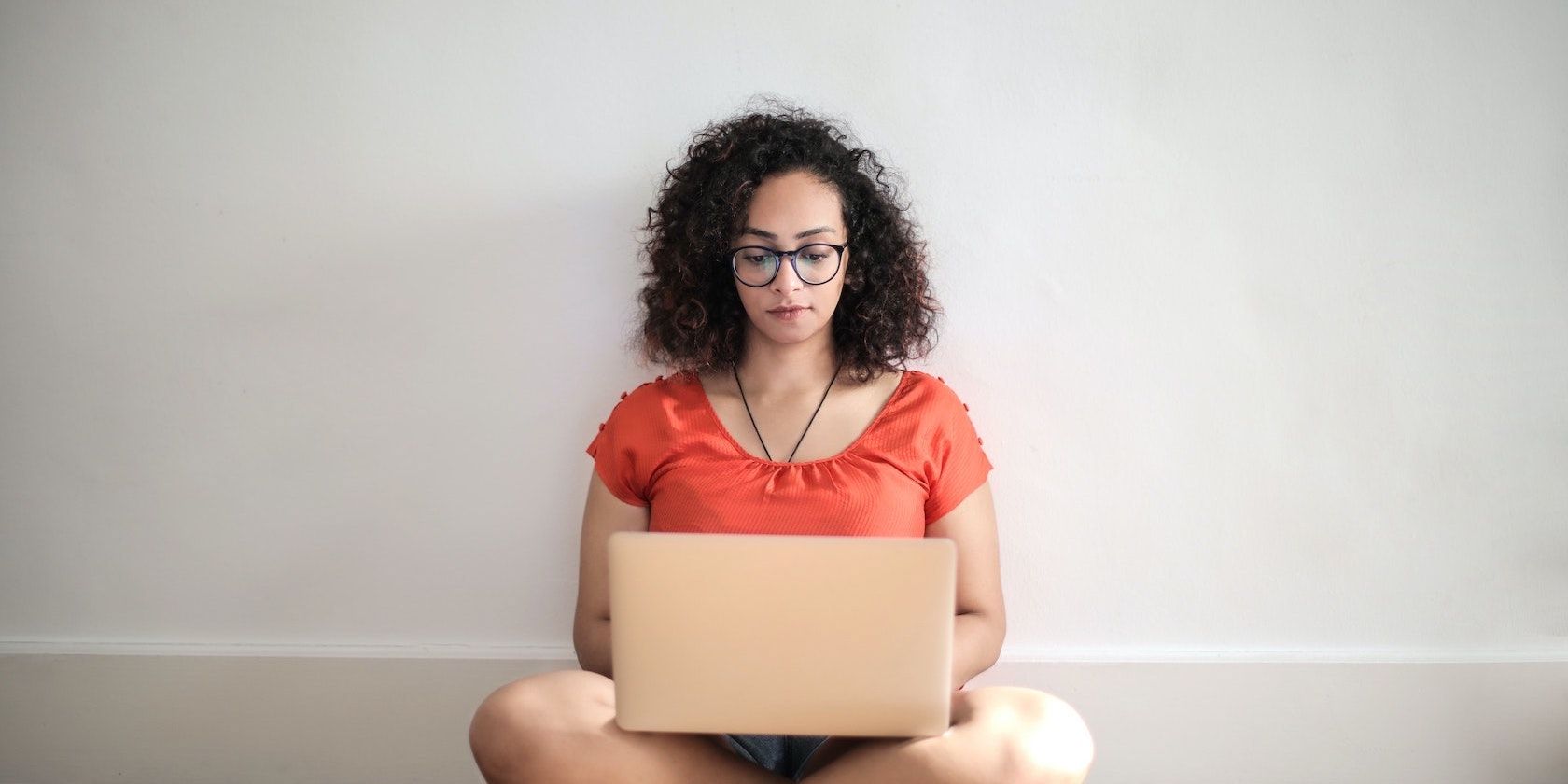 A woman sitting cross-legged on the floor, facing the camera, with a laptop on her knees.