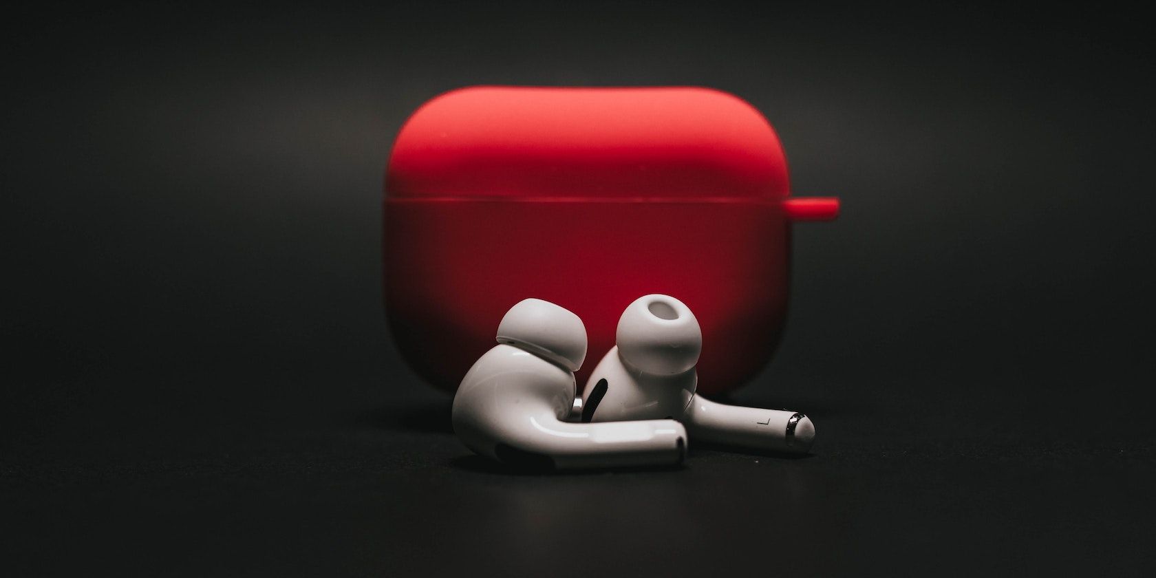 White AirPods With a Red Case on a Black Background