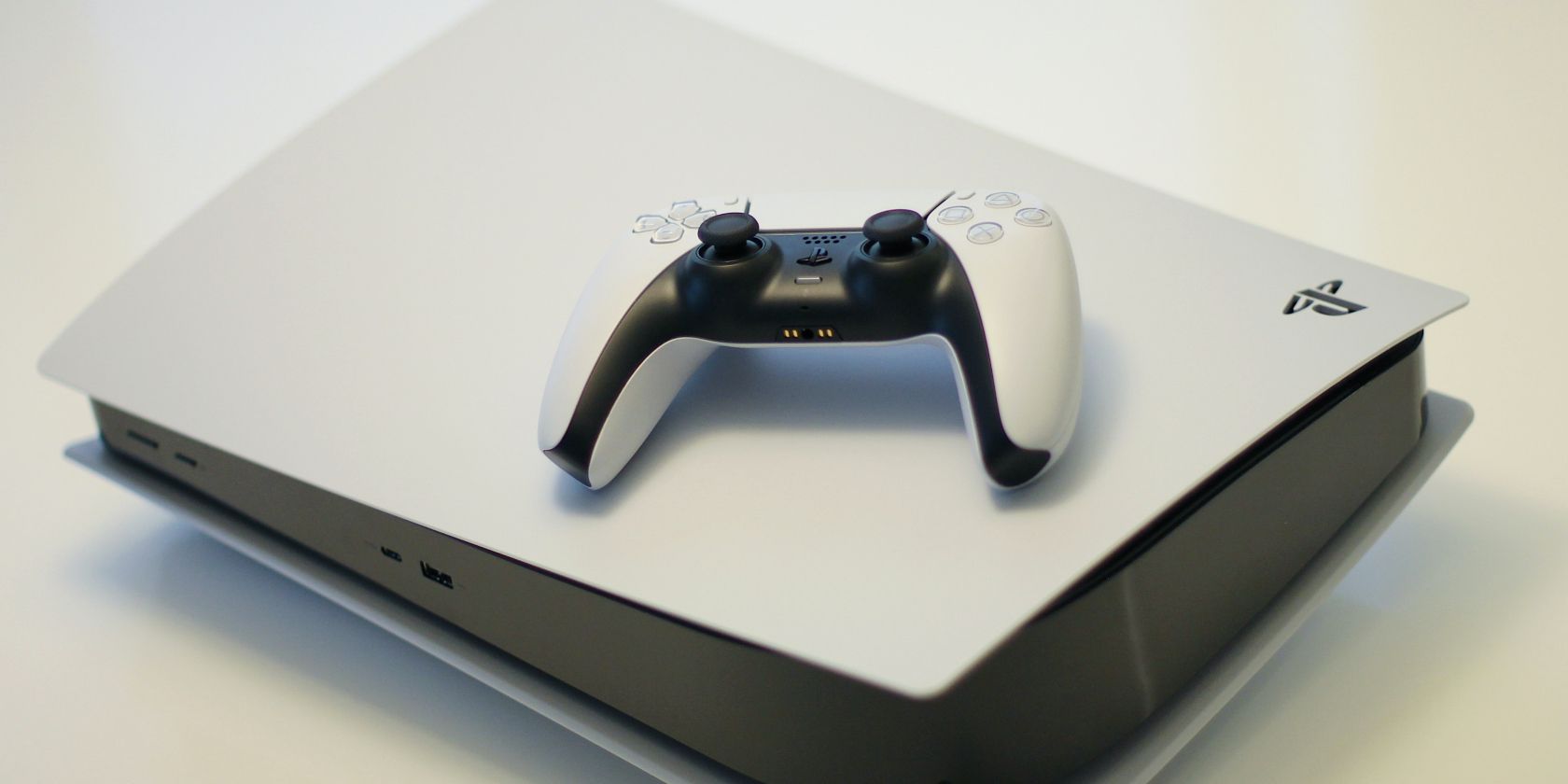White PS5 lying horizontally with a white controller on top of it