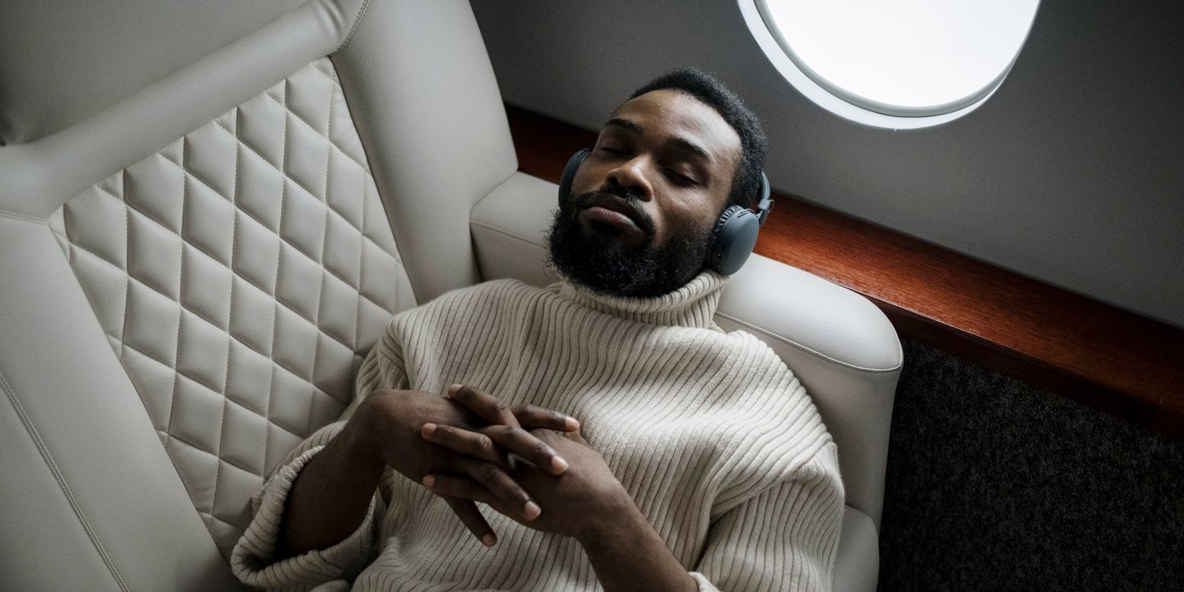 A man in white pullover sitting in a white chair listening to headphones
