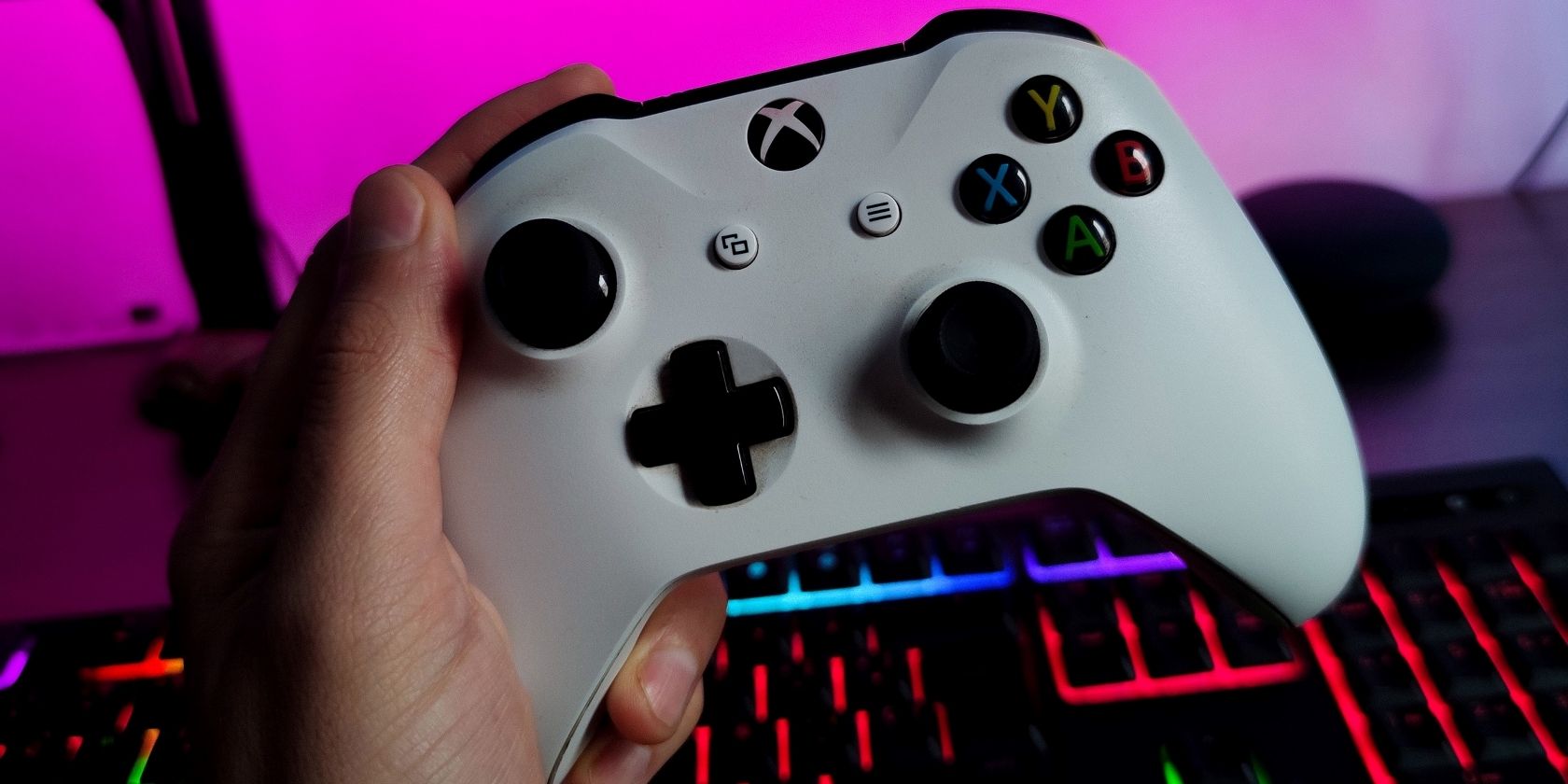 A photograph of a person holding a white Xbox One controller in front of a monitor