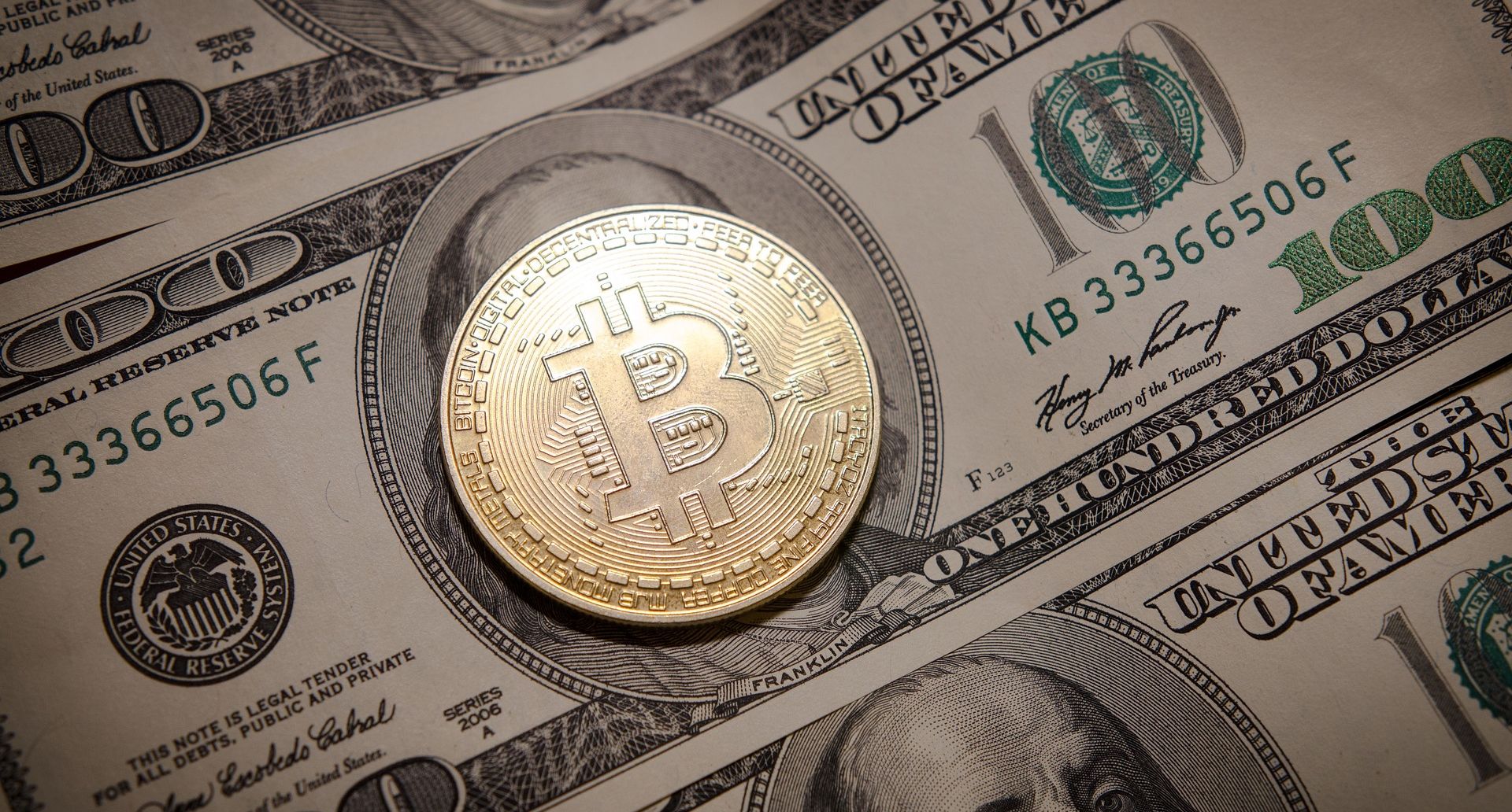 bitcoin laid on top of hundred dollar bill