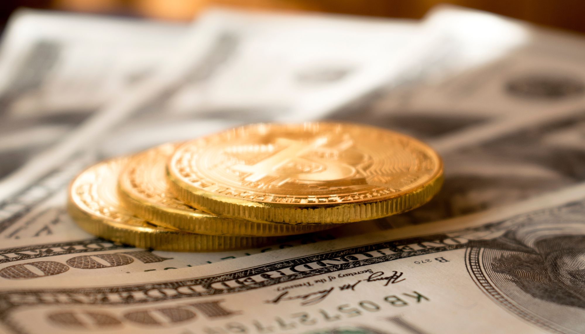 gold bitcoins lying on hundred dollar bills
