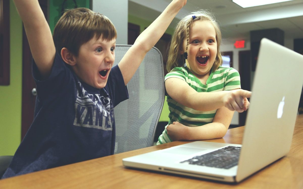 Two children are laughing while looking at the laptop