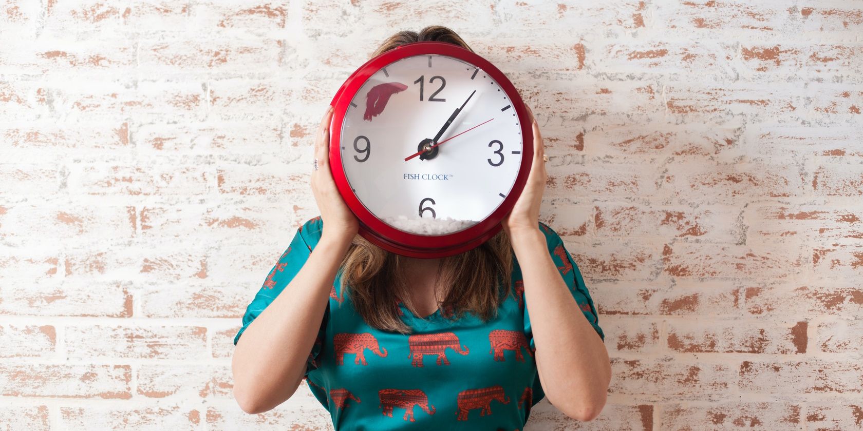 A woman holding a clock to her face