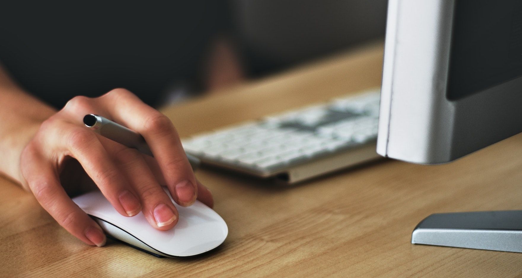 Uma mão segurando o mouse de um computador desktop 