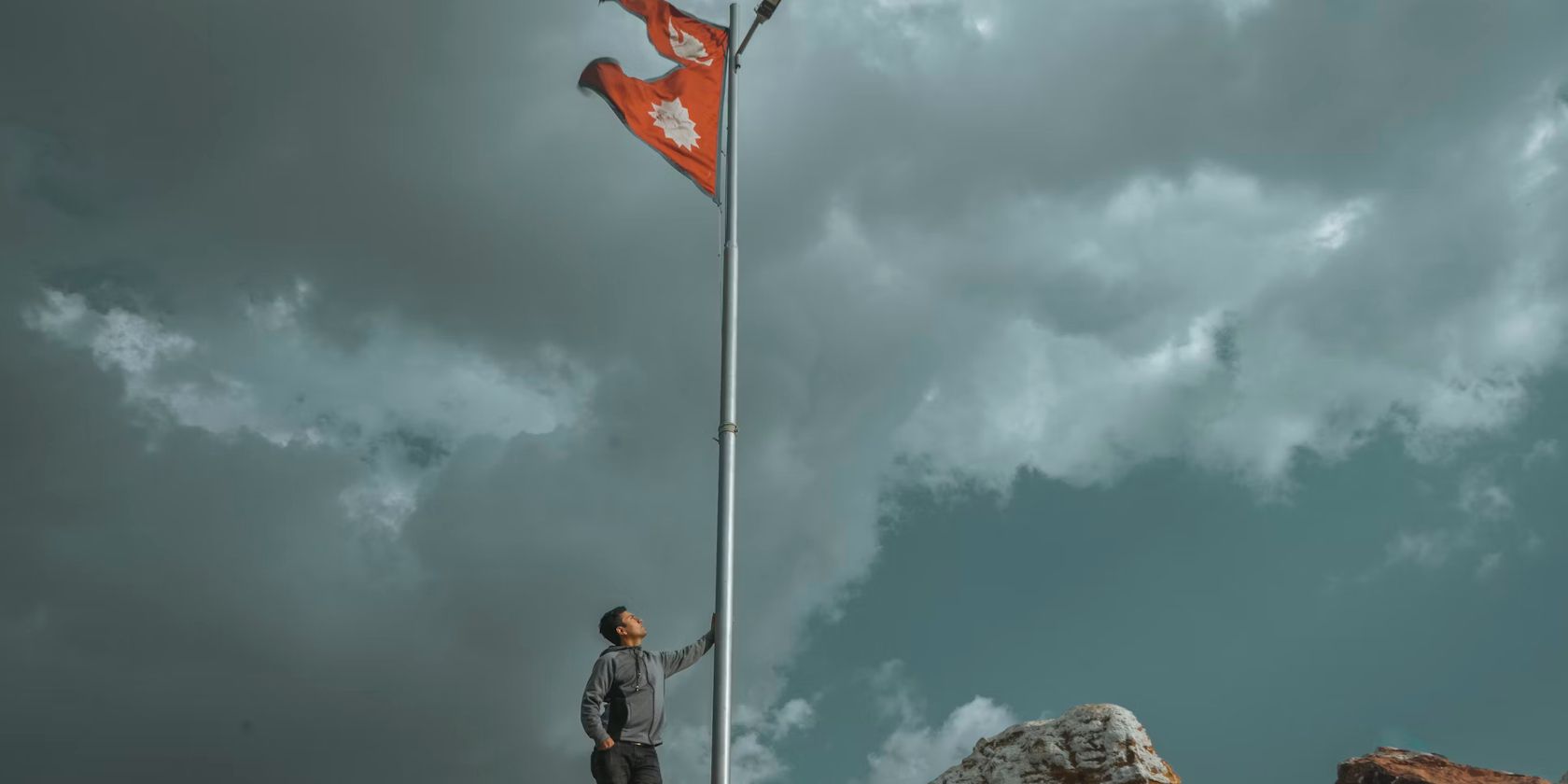 man at the base of a flagpole flying the flag of nepal