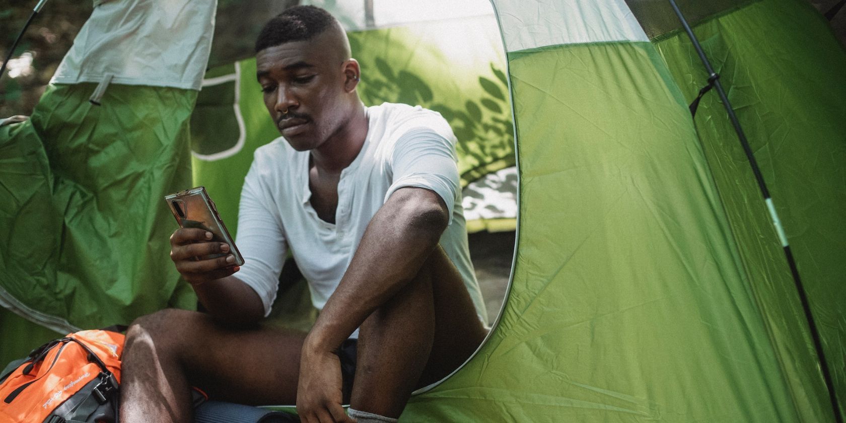 Man outdoors in camping tent distracted by smartphone